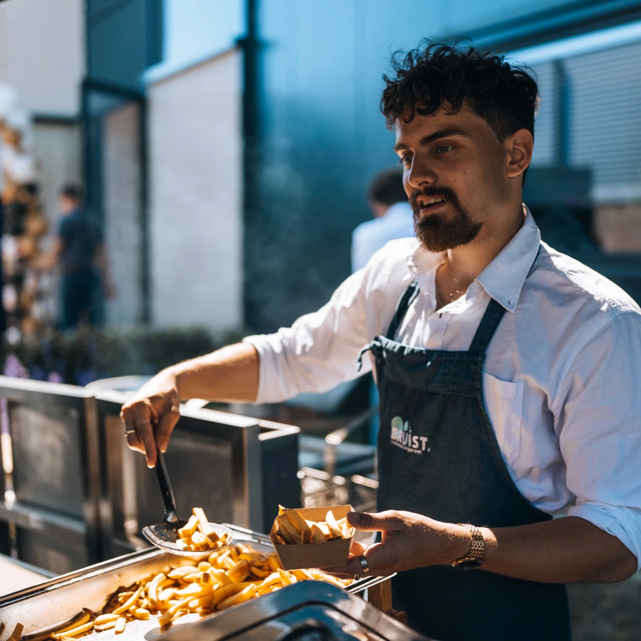 een man die friet opschept in een kartonnen bakje bij een foodtruck