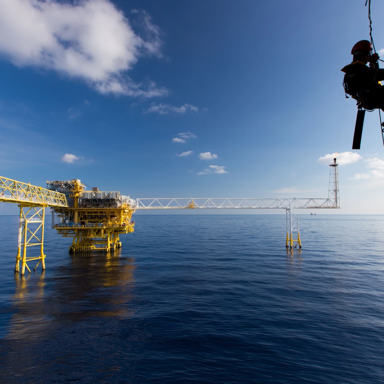 man aan touw hangend bij water met helm