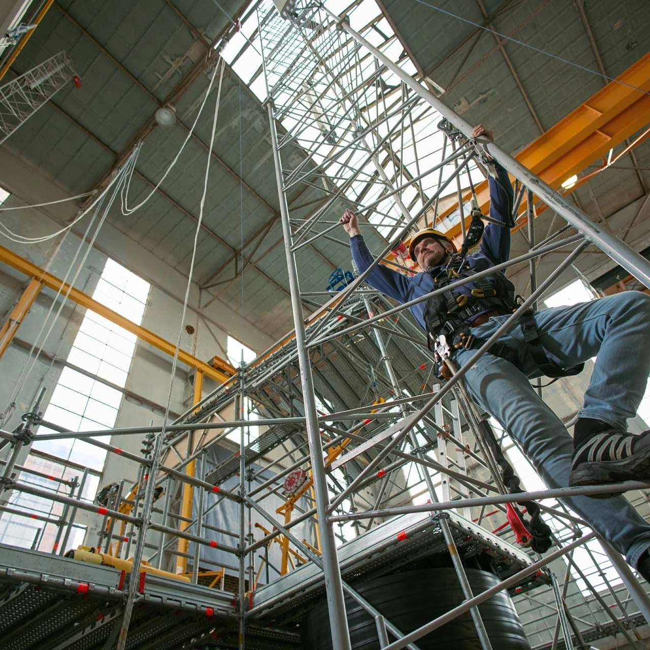 man die ladder beklimd in loods met helm en harnas