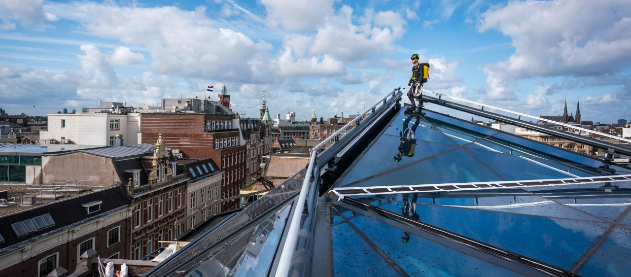 een man die op een glazen dak staat aangelijnd aan een railsysteem, geheel op maat gemaakt