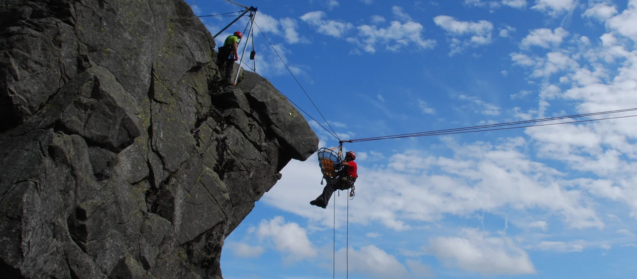 grote rots met man hangend in touw met helm en brancard