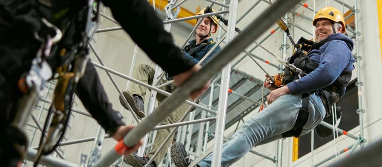 personen op hoogte hangend aan touw met helm op en harnas aan