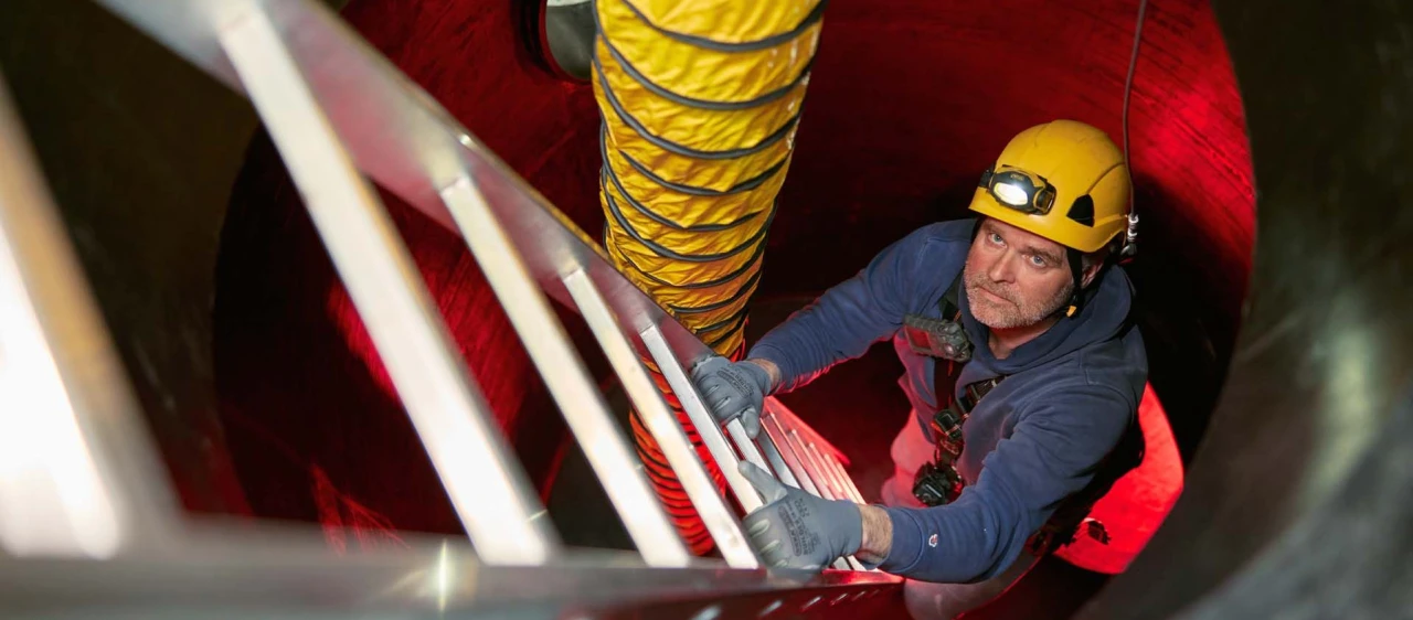 man die ladder op klimt in besloten ruimte met helm en lamp op hoofd