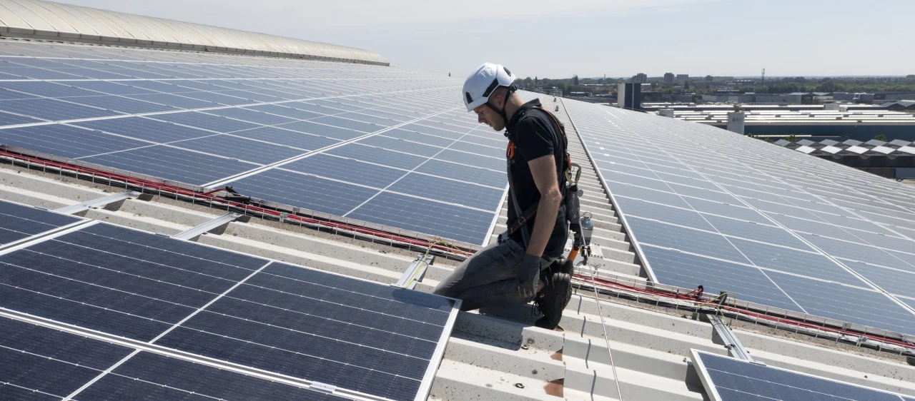 een man die op een dak zit op zijn knieën naast zonnepanelen