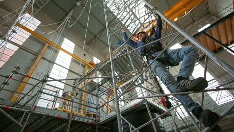 man op ladder in loods met harnas en helm