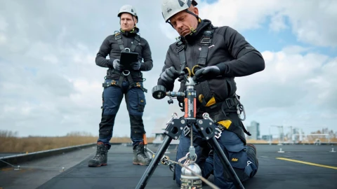 mannen op dak met apparatuur en helm op en harnas aan
