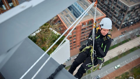 man hangend aan gebouw aan touw met helm op en in harnas