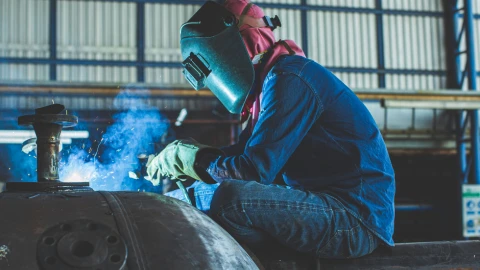 een persoon die met een kap op en handschoenen aan staat te lassen