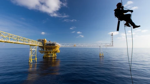 man aan touw hangend bij water met helm