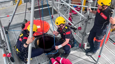 een aantal personen met een shirt aan van de marine brandweer die om een besloten ruimte staan om een slachtoffer te redden