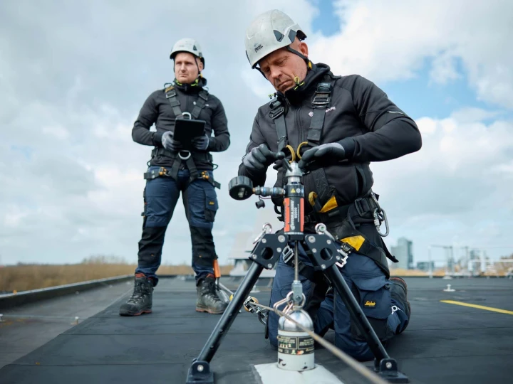 mannen op dak met apparatuur en helm op en harnas aan