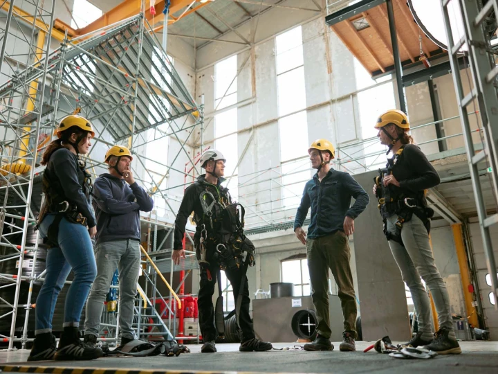 personen in rij in loods met helm en harnas